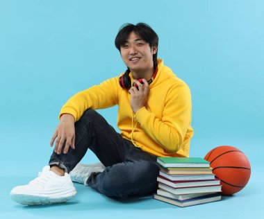 Kitapları ve açık mavi arka planda basketbol topu olan bir öğrenci.