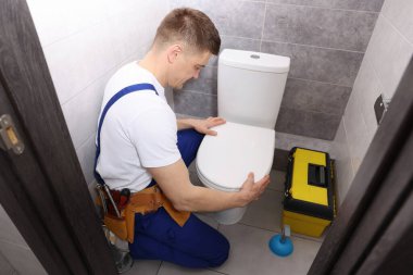 Profesyonel tesisatçı tuvaletteki klozeti tamir ediyor.