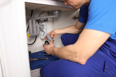 Tesisatçı, lavabonun altındaki boruları tamir ediyor. Kapalı.