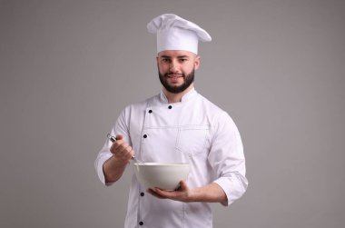 Üniformalı mutlu pastacı açık gri arka planda çırpı ve kase tutuyor.