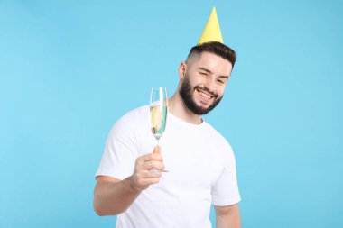 Doğum günün kutlu olsun. Açık mavi arka planda parti şapkası ve bir bardak şampanyası olan yakışıklı bir adam.