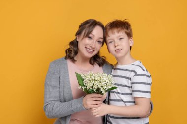 Çocuk sarı arka planda annesine güzel bir çiçek buketi veriyor.