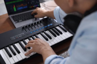 İçerideki masada MIDI klavyesi ve dizüstü bilgisayarıyla çalışan adam, seçici odaklanma