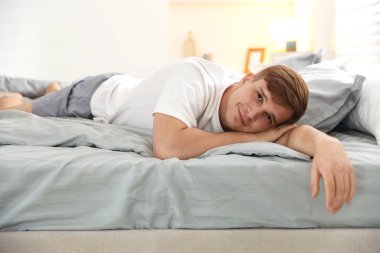 Genç adam evde yumuşak bir döşekle yatakta yatıyor.