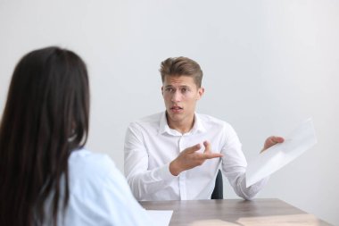 Ahşap masada oturan genç bir adam kadınlara şikayette bulunuyor.