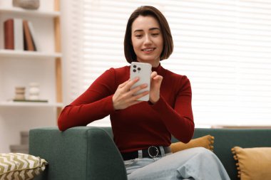 Evdeki koltukta modern akıllı telefon kullanan bir kadın.