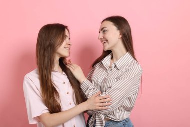 Arkadaşlar pembe arka planda birbirlerine sarılıyorlar.