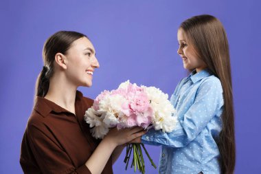 Şirin küçük kız annesine mor arka planda bir buket güzel şakayık veriyor.