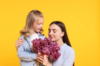 Anne ve kızı sarı arka planda bir demet leylak çiçeğiyle