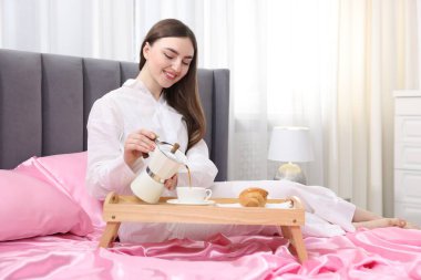 Gülümseyen kadın kahve dolduruyor Moka çaydanlığından yatağa pembe ipek çarşaflarla.