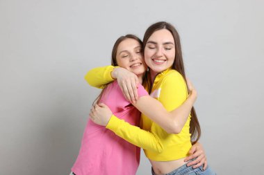 Arkadaşlar açık gri arka planda birbirlerine sarılıyorlar.