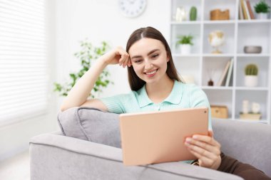 Evdeki koltukta modern tablet kullanan genç bir kadın.