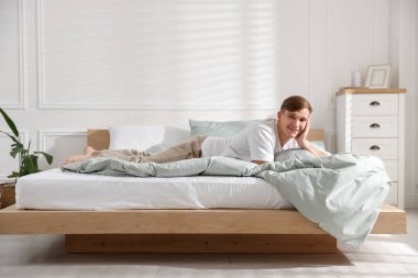 Genç adam evde yumuşak bir döşekle yatakta yatıyor.