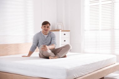 Genç adam evinde yumuşak bir yatakla yatakta oturuyor.