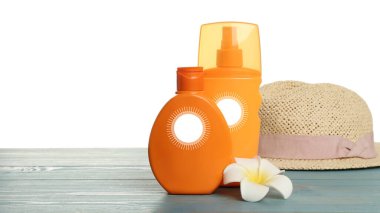 Güneş kremi ürünleri ve plaj şapkası ahşap masada beyaz arka planda. Güneş çizimleri olan şişeler.