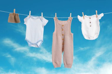 Mavi gökyüzüne karşı çamaşır ipinde kurumuş farklı bebek kıyafetleri.