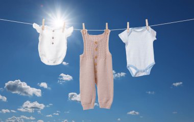 Mavi gökyüzüne karşı çamaşır ipinde kurumuş farklı bebek kıyafetleri.