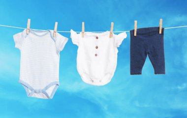 Mavi gökyüzüne karşı çamaşır ipinde kurumuş farklı bebek kıyafetleri.