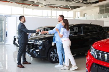 Satıcı salonda mutlu bir aileye araba anahtarı veriyor.