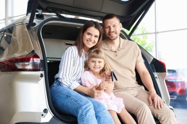 Anahtarları olan mutlu aile salonda arabanın bagajında oturuyor.