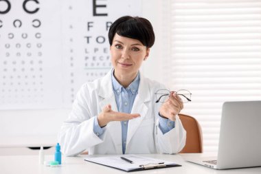 Klinikteki beyaz masada gözlüklü profesyonel göz doktorunun portresi.