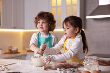 Yemek tarifi. Sevimli çocuklar mutfaktaki masada kurabiye hamuru karıştırıyor.