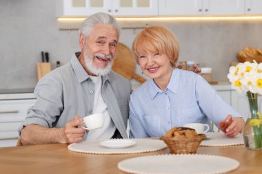 Mutfaktaki ahşap masada birlikte kahvaltı eden sevimli yaşlı çift.