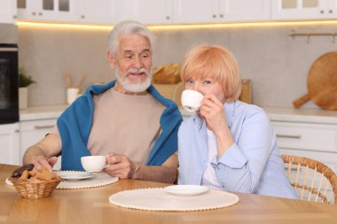 Mutfaktaki ahşap masada birlikte kahvaltı eden sevimli yaşlı çift.
