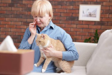 Yaşlı kadın evdeki kanepede kedisiyle alerji geçiriyor.