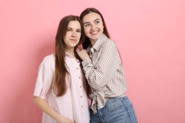 Arkadaşlar pembe arka planda birbirlerine sarılıyorlar.