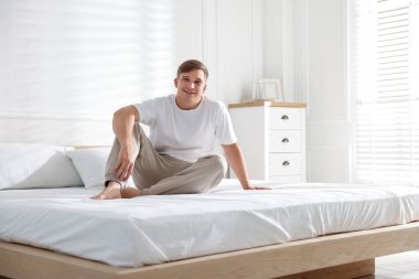 Genç adam evde yumuşak bir döşekle yatakta yatıyor.