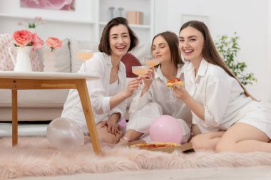 Pijamalı, alkollü mutlu arkadaşlar evde yerde pizza yiyorlar.