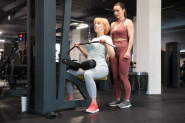 Spor salonunda profesyonel antrenör tarafından yönetilen son sınıf kadın çekme makinesi eğitimi.