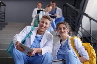 Bir grup tıp öğrencisi merdivenlerde kapalı, düşük açılı üniformalarla.