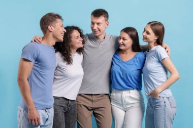 Açık mavi arka planda kucaklaşan arkadaş grubu