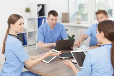 Üniformalı tıp öğrencileri kapalı bir masada birlikte çalışıyorlar.