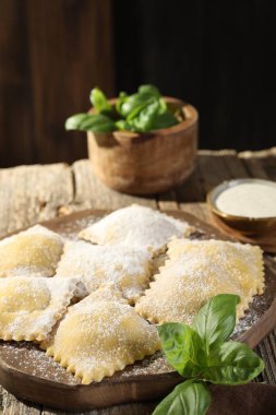 Ahşap masada pişmemiş ravioli ve fesleğen, yakın plan.