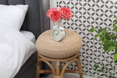 Çalar saati olan yan masa ve yatağın yanında çiçekler.