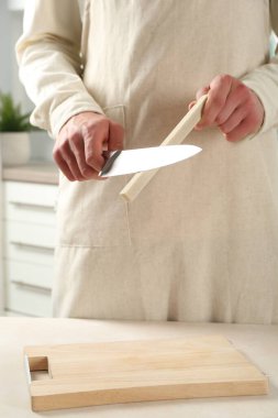 Kapalı alanda bej masa bileyicisiyle bıçak bileyen bir adam.