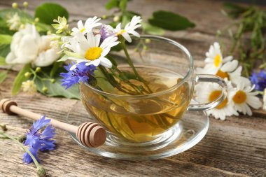 Cam bardakta Aromatik bitki çayı, tahta masada çiçekler ve kepçe, yakın plan.