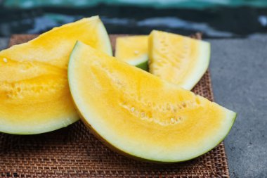 Olgun sarı karpuz parçaları hasır masada, yüzme havuzunun yanında, yakın plan.