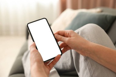 Evdeki koltukta modern akıllı telefon kullanan bir kadın.