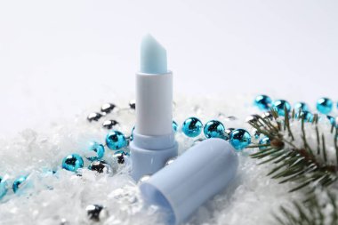 Nemlendirici dudak kremi, Noel dekorasyonu ve yapay kar üzerindeki köknar ağacı dalları, yakın plan. Kış bakımı