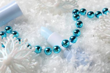 Nemlendirici dudak kremi ve yapay kar üzerine Noel süsü, yakın plan. Kış bakımı