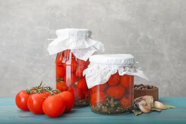 Kavanozlarda salamura domates, taze ürünler ve baharatlar açık mavi ahşap masa üzerinde gri arka plan, yakın plan