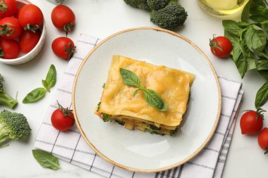 Lezzetli bir parça vejetaryen lazanya ve malzemeler beyaz masada, düz yerde.