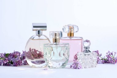 Açık gri arka planda leylak çiçekli parfüm şişeleri ve dallar, yakın plan.