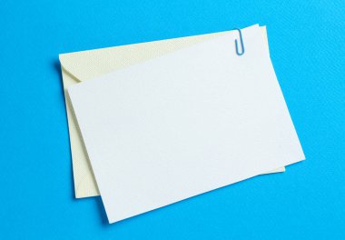 Açık mavi arka planda boş davetiye ve zarf, üst manzara. Tasarım için boşluk