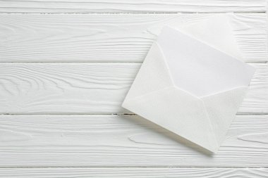 Beyaz ahşap masa üzerinde boş davetiye ve zarf, üst manzara. Metin için boşluk