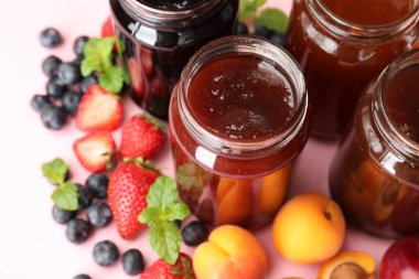 Açık pembe arka planda farklı kavanozlar ve malzemeler, yakın plan.